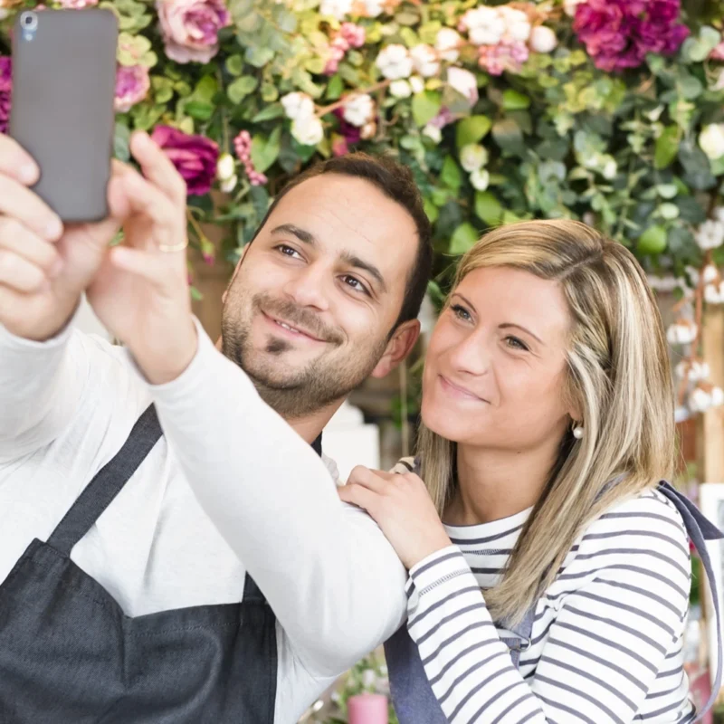 Two florists in flower shop, taking an Instagram selfie, using smartphone