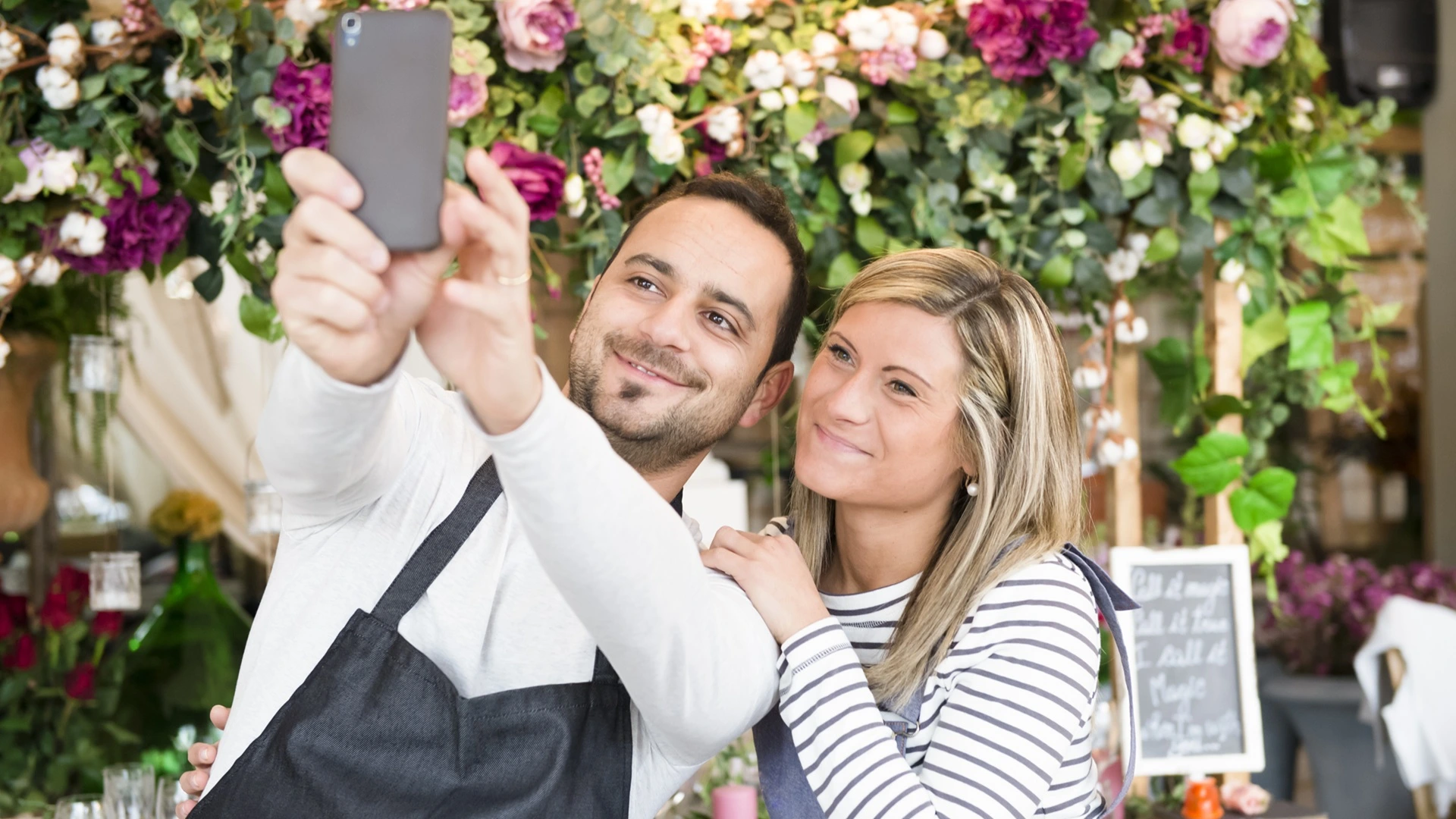 Two florists in flower shop, taking an Instagram selfie, using smartphone